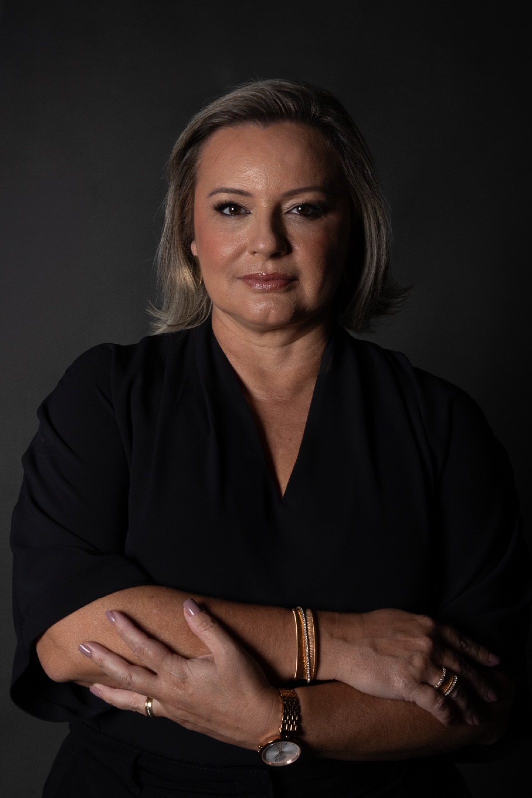 Fabiana Carvalho, fundadora da Valense, em retrato de estúdio: blusa preta, braços cruzados e olhar sereno sobre fundo escuro